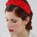 Close-up of a model with her eyes closed, showcasing the Watermelon Headband, featuring red silk crepe fabric with white polka dots and an elegant gold logo detail.