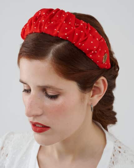 Close-up of a model with her eyes closed, showcasing the Watermelon Headband, featuring red silk crepe fabric with white polka dots and an elegant gold logo detail.