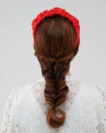 Rear view of a model with auburn hair in a braid, adorned with the Watermelon Headband in red with white polka dots, against the delicate lace backdrop of the Maria Lily Mini-Dress.