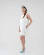 Model poses in a crisp white Maria Daisy Mini Dress and colorful Tulip Headband, paired with chic light blue heels against a clean, white background.