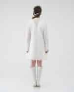 Rear view of a model in a white lace Maria Lily Mini Dress with intricate sequin embroidery and deep V-back, paired with a Lemon Headband and white boots.