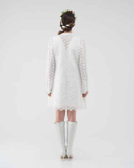 Rear view of a model in a white lace Maria Lily Mini Dress with intricate sequin embroidery and deep V-back, paired with a Lemon Headband and white boots.