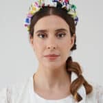 Front view of a model showcasing the vibrant Lemon Headband with colorful floral patterns, set against her braid and the white lace of the Maria Lily Mini Dress.