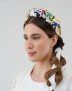 Close-up side profile of a model wearing the Lemon Headband with an exuberant floral pattern, accenting her twisted braid and the textured white lace overlay of her dress.