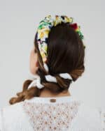 Rear view of a model wearing a Lemon Headband with white ribbon braided into her hair, above a white lace dress with a 'Maria' metal tag.