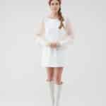 A woman stands facing the camera wearing the Maria Peony Mini Dress, a white dress with sheer balloon sleeves, paired with the vibrant Fern Headband and white knee-high boots