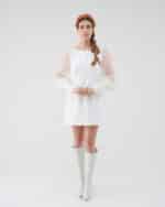A woman stands facing the camera wearing the Maria Peony Mini Dress, a white dress with sheer balloon sleeves, paired with the vibrant Fern Headband and white knee-high boots