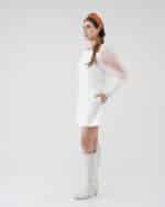 Side profile of a woman modeling the Maria Peony Mini Dress, complete with sheer balloon sleeves and a sleek design, complemented by the Fern Headband and stylish white knee-high boots.