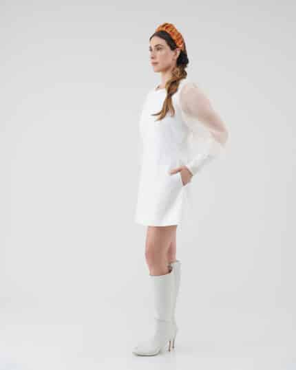Side profile of a woman modeling the Maria Peony Mini Dress, complete with sheer balloon sleeves and a sleek design, complemented by the Fern Headband and stylish white knee-high boots.
