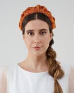 Front view of a woman with a side braid, wearing the Maria Fern Headband in a vibrant red and yellow pattern.