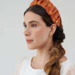 Side profile of a woman showcasing the Maria Fern Headband with an intricate red and yellow pattern, paired with a casual white blouse and a loose side braid.