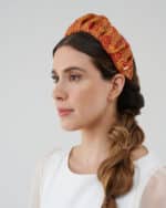Side profile of a woman showcasing the Maria Fern Headband with an intricate red and yellow pattern, paired with a casual white blouse and a loose side braid.