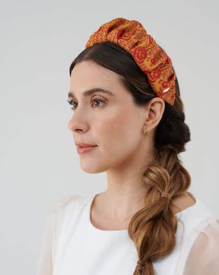 Side profile of a woman showcasing the Maria Fern Headband with an intricate red and yellow pattern, paired with a casual white blouse and a loose side braid.