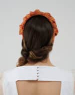 Rear view of a woman wearing the Maria Fern Headband, displaying its vibrant red and yellow fabric, and the Maria Peony Mini Dress with delicate white button details on the back.