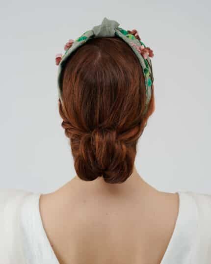 Rear view of the Greenery Headband with hand-embroidered details and a model's twisted low bun hairstyle, complemented by the elegant Maria Jasmine Mini Dress.