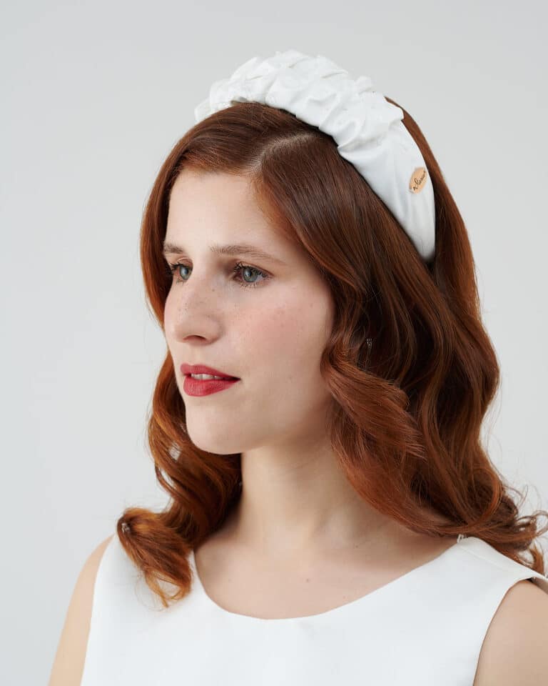 Side view of a woman with auburn hair and red lipstick, wearing a white Daisy Headband.