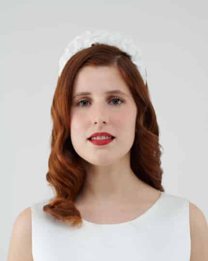 Frontal view of a smiling woman with auburn hair wearing a white Daisy Headband.