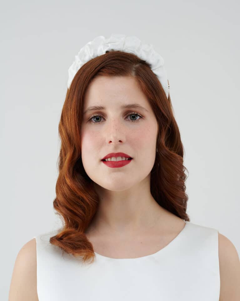 Frontal view of a smiling woman with auburn hair wearing a white Daisy Headband.