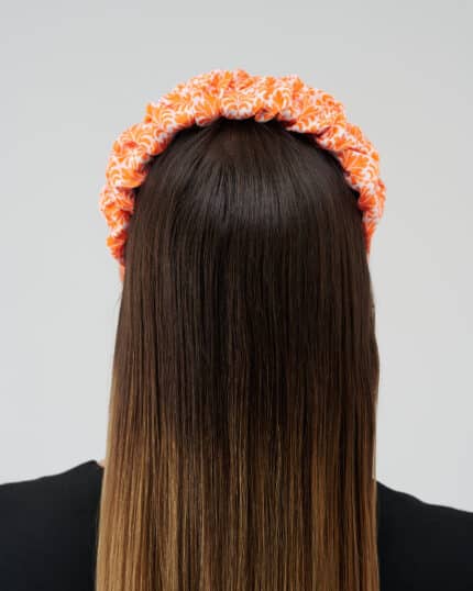 Rear view of a woman wearing the Maria Coral Headband with a rich orange and white floral print, over long, straight brown hair.