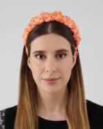 Portrait of a woman with long, straight brown hair wearing the Maria Coral Headband, featuring a bright coral color with an intricate white floral pattern