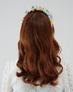 Rear view of a woman with auburn hair wearing the Tulip Headband, featuring a vibrant silk devoré fabric, against the backdrop of the white Maria Lily Mini Dress with lace detail.