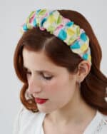 Close-up of a woman with auburn hair and red lipstick wearing the Tulip Headband, made with multicolored silk devoré fabric.