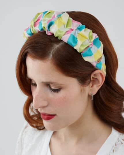 Close-up of a woman with auburn hair and red lipstick wearing the Tulip Headband, made with multicolored silk devoré fabric.