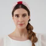 Model facing forward wearing the Strawberry Headband with red crystal bead details and a bold red bow atop a polka-dot fabric, paired with the Maria Jasmine Mini Dress.