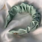 Soft pastel green satin headband with an engraved 'Maria' metal plaque, presented on a silky white surface.