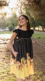 Model outdoors gazing away with a joyful expression, showcasing the Maria Terceira Mini-Dress in black with a floral-patterned yellow hem from Maria Atelier's Summer Special Edition.