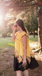Model in profile wearing sunglasses, the yellow Maria Terceira Mini-Dress with black floral accents from Maria Atelier's Summer Special Edition, holding a black clutch.