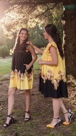 Two models enjoying a sunlit park, both wearing Maria Terceira Mini-Dresses from Maria Atelier's Summer Special Edition, one in black and the other in yellow with floral designs.