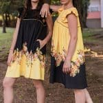 Two models standing back-to-back in a wooded area, wearing the Maria Terceira Mini-Dresses in yellow and black with floral designs, from the Maria Atelier Summer Special Edition.