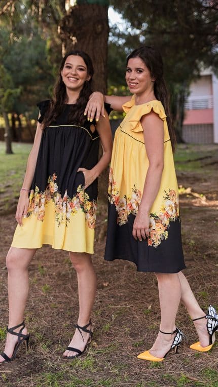 Two models standing back-to-back in a wooded area, wearing the Maria Terceira Mini-Dresses in yellow and black with floral designs, from the Maria Atelier Summer Special Edition.