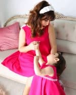 Heartwarming scene of a mother in a fuchsia dress with white Daisy Headband playing with her daughter, who wears a matching dress, in an elegantly furnished room.
