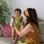 A mother in a brocade dress smiles at her gleeful baby, clad in a matching lime outfit with brocade accents, highlighting their close bond and the intricate design of the Maria Peggy Special Edition Mommy & Me dresses.
